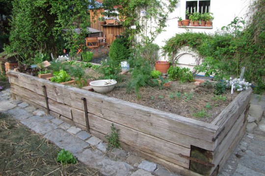 Langes Hochbeet aus Holz mit angebautem Gemüse und Töpfen vor einem Haus | © Birgit Helbig