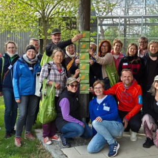Gruppe von Menschen im Freien hält LBV-Schilder, lächelt und trägt grüne Taschen. Hintergrund: Glasgebäude und Bäume.