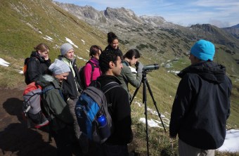 Exkursionsgruppe mit sieben Teilnehmern und dem Exkursionsleiter stehen auf einem Berg, ein Teilnehmer schaut durch ein Spektiv | © Henning Werth