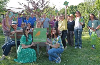 Eine Gruppe von Menschen steht im Garten und hält LBV-Schilder für einen vogelfreundlichen Garten in die Kamera.