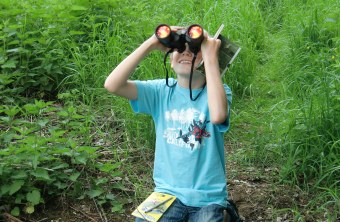 Junge sitzt am Boden und beobachtet mit einem Fernglas Vögel | © Marion Brunner