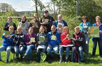 Gruppe von Menschen im Freien hält LBV-Schilder für vogelfreundliche Gärten hoch, lächelnd in einem grünen Park.