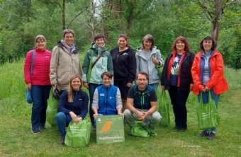 Gruppe von Menschen im Freien mit LBV-Taschen, hält ein Schild "Vogelfreundlicher Garten" in einem grünen Park.