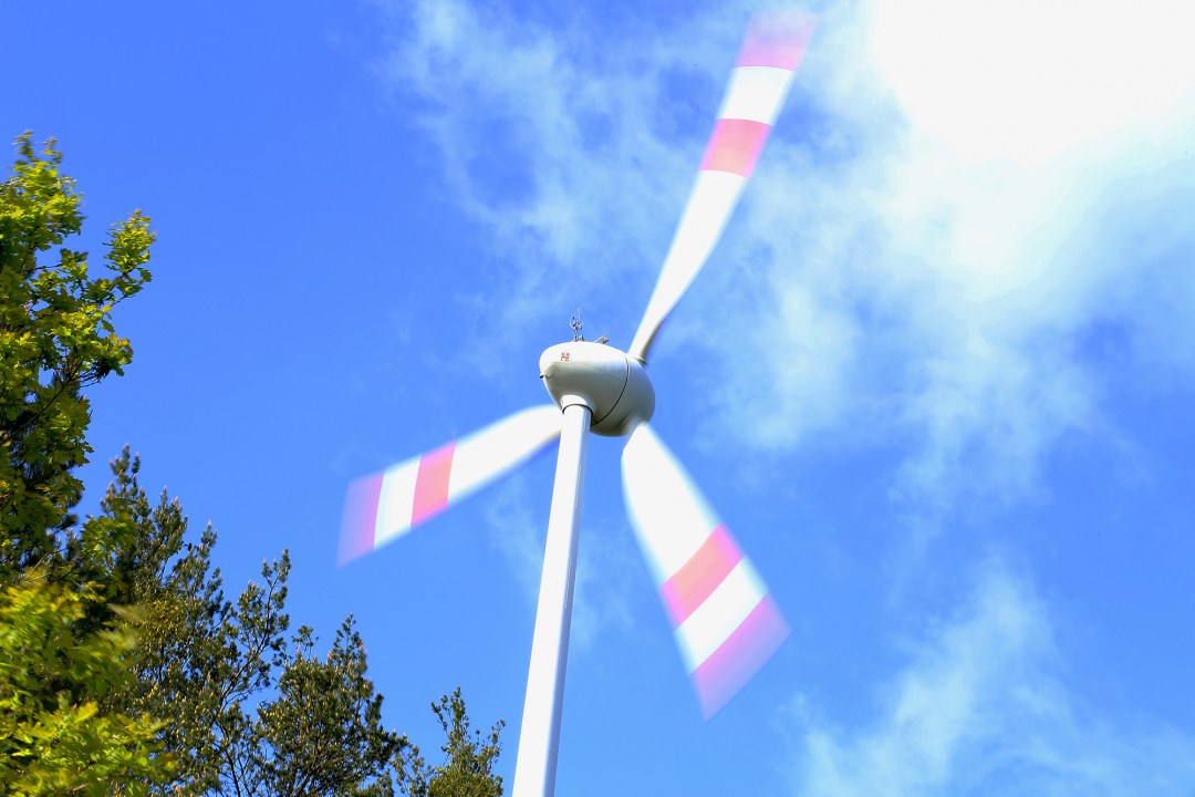 Windrad mit drei Rotorblättern die jeweils zwei rote Streifen haben, daneben scheinen Bäume zu stehen | © Peter Bria