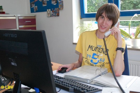 Christoph sitzt an einem Schreibtisch hinter einem PC und telefoniert