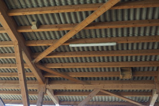 Holzdachkonstruktion mit Wellenblech und Schwalbenwinkeln und Schwalbenboxen, darunter eine Leuchtstoffröhre | © Rieke Wüpping