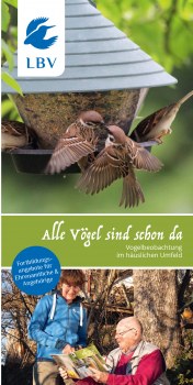 Eine Gruppe von Vögeln versammelt sich an einem Futterhaus, während zwei Personen im Freien den LBV-Flyer betrachten.