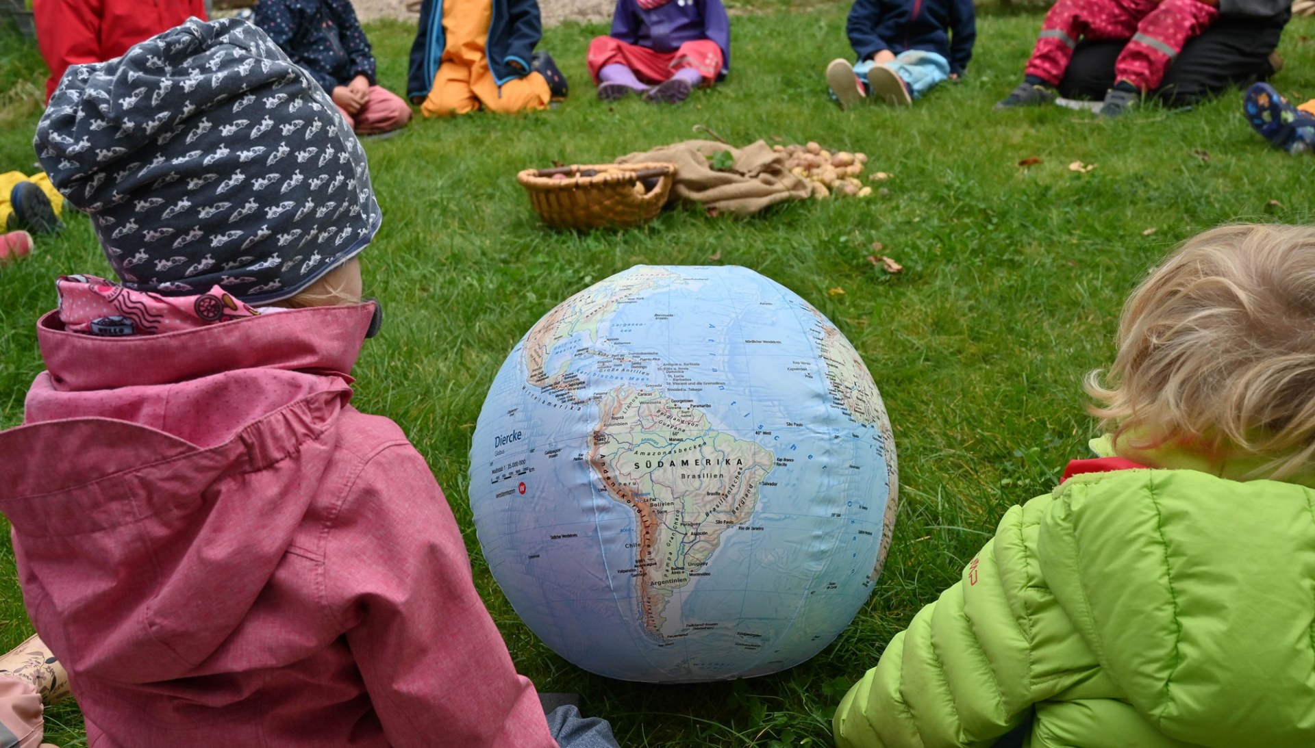 Zwei Kinder sitzen in der Wiese und betrachten einen Erdball | © Tobias Tschapka