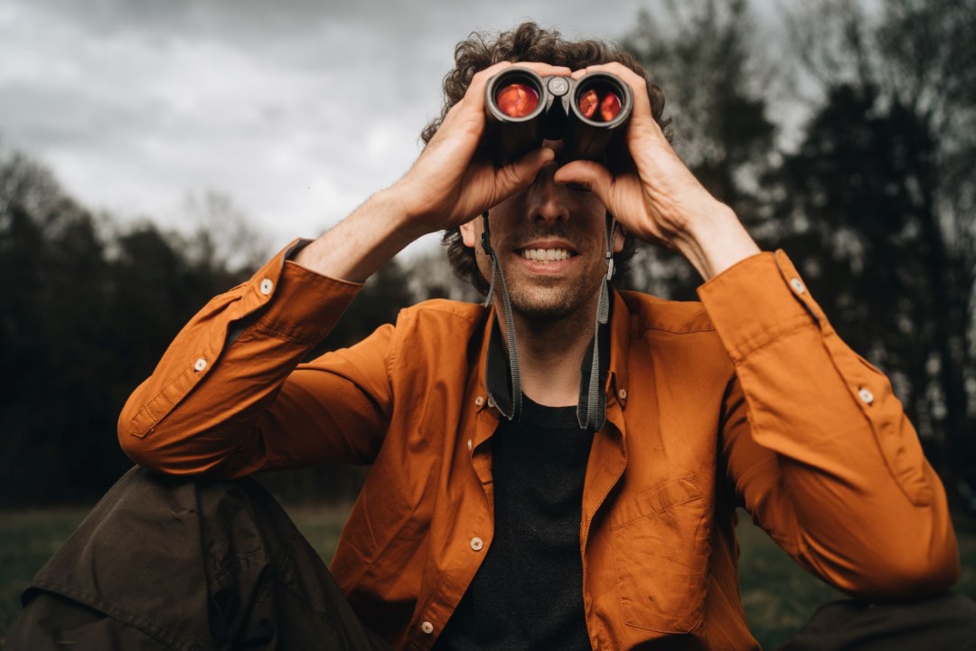 Philipp sitzt auf dem Boden und schaut durch ein Fernglas, Foto von vorne |©AlexeyTestov