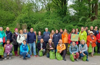 Gruppe von Menschen im Freien mit LBV-Taschen vor grüner Kulisse. Sie halten ein Schild "Vogelfreundlicher Garten".
