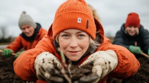 Eine Frau in orangefarbener Mütze pflanzt bei einer Teamaktion Setzlinge in die Erde. | © stock.adobe.com