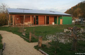 Holzgebäude mit Solardach und Gartenweg im Vordergrund, genutzt von LBV für Umweltaktivitäten.