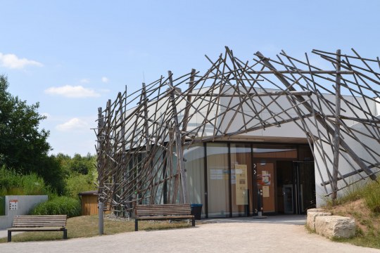Umweltstation am Rothsee. Links das Gebäude, wo ein gepflasterter Weg hinführt. Rechts befindet sich eine Wiese mit zwei Tischen und Bänken drumherum. Außerdem neu gepflanzte Bäume | © L. Hauselt