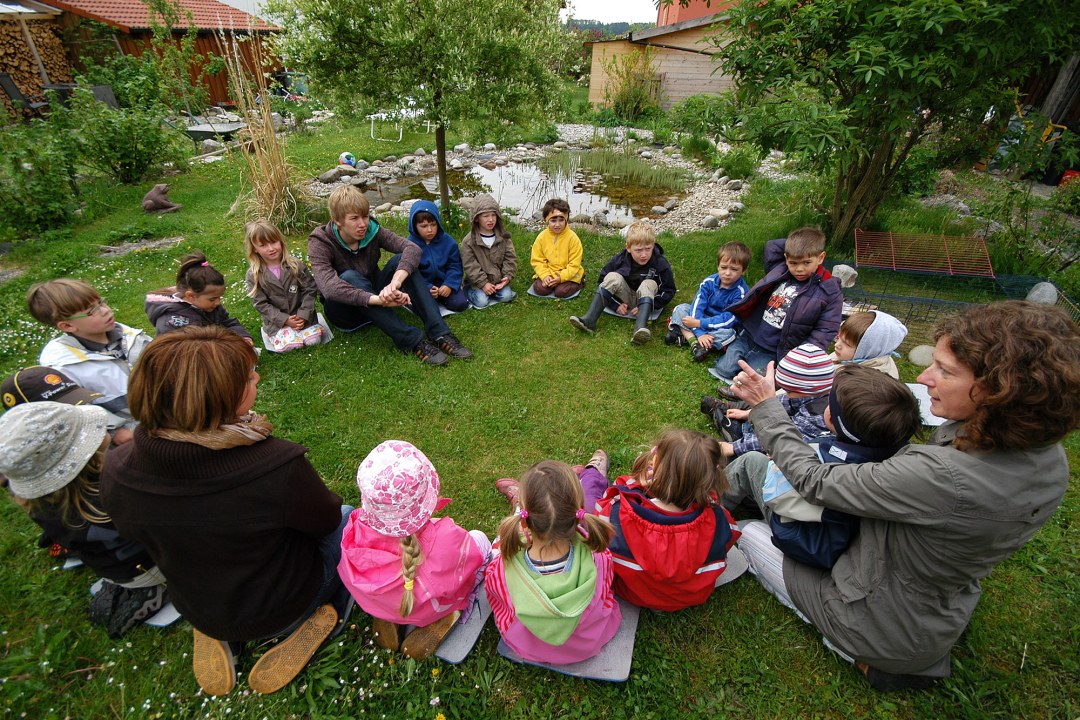 Kinder des Arche-Noah-Kindergartens sitzen draußen im Kreis auf einer Wiese | © Horst Munzig