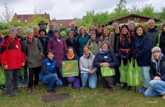 Gruppe von Menschen posiert draußen mit LBV-Schild "Vogelfreundlicher Garten", umgeben von grüner Natur.