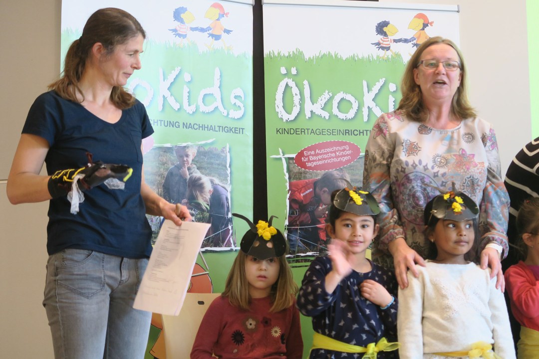 Kinder stehen als Bienen verkleidet auf einem Podium, im Hintergrund ist mit einem Projektor das Logo der Ökokids und das aktuelle Datum "21.11.2017" an die Wand geworfen | © Norbert Schäffer