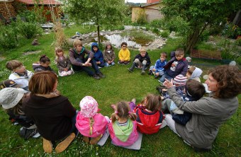 Kinder des Arche-Noah-Kindergartens sitzen draußen im Kreis auf einer Wiese | © Horst Munzig