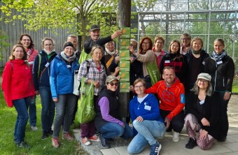 Gruppe von Menschen im Freien hält LBV-Schilder, lächelt und trägt grüne Taschen. Hintergrund: Glasgebäude und Bäume.