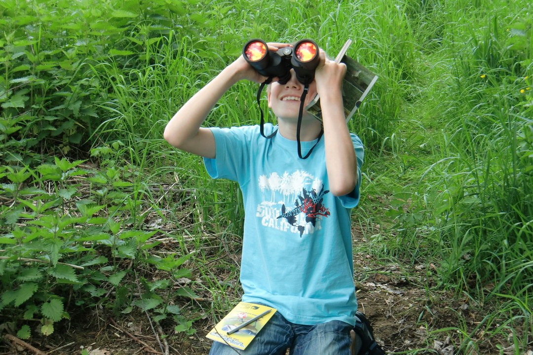 Junge sitzt am Boden und beobachtet mit einem Fernglas Vögel | © Marion Brunner