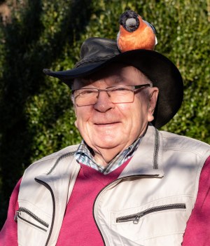 Ein älterer Herr trägt einen Hut mit einem Plüschgimpel darauf, passend zum Engagement des LBV für Naturschutz.
