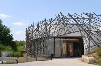 Umweltstation Rothsee vor blauem Himmel im Sommer. Davor zwei Bänke und ein gepflasterter Weg | © L. Hauselt