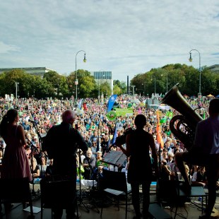 Auftritt von Hans Well mit den Wallbappn bei Demo Mia ham's satt von der Bühne aus fotografiert, man sieht die großen Menschenmassen auf dem Königsplatz und im Vordergund die Silhouetten der vier Musiker | © LBV