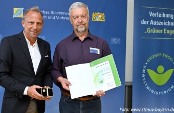 Zwei Männer präsentieren stolz eine Urkunde und Medaille der Auszeichnung "Grüner Engel" für Naturschutz in Bayern.
