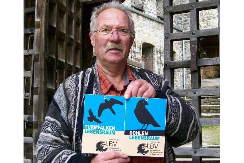 Adolf Geismayr mit der verliehenen Plakette "Lebensraum Kirchturm" vor der ausgezeichneten Burgruine Sulzberg | © LBV